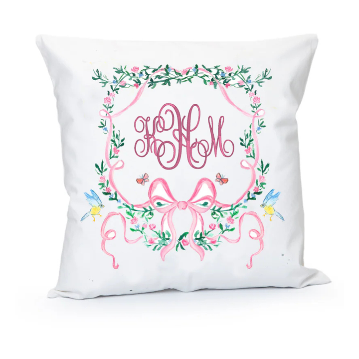 Decorative pillow with floral wreath and pink monogram on a white background