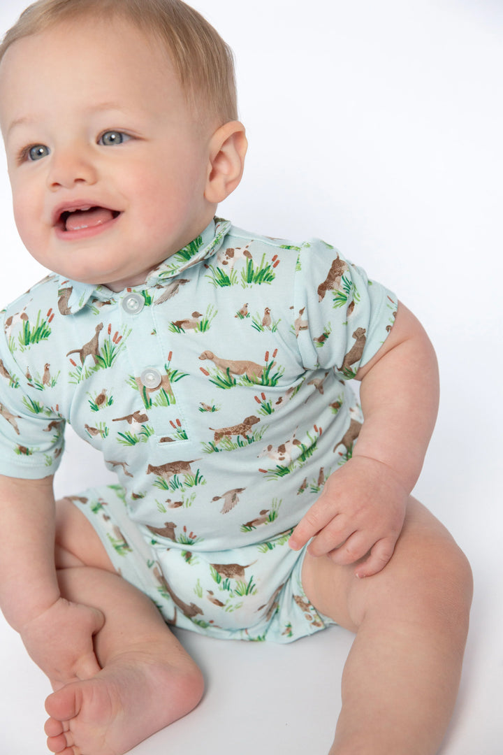 A baby wearing a short-sleeve light blue-green romper with a woodland animal print, sitting against a plain white background.