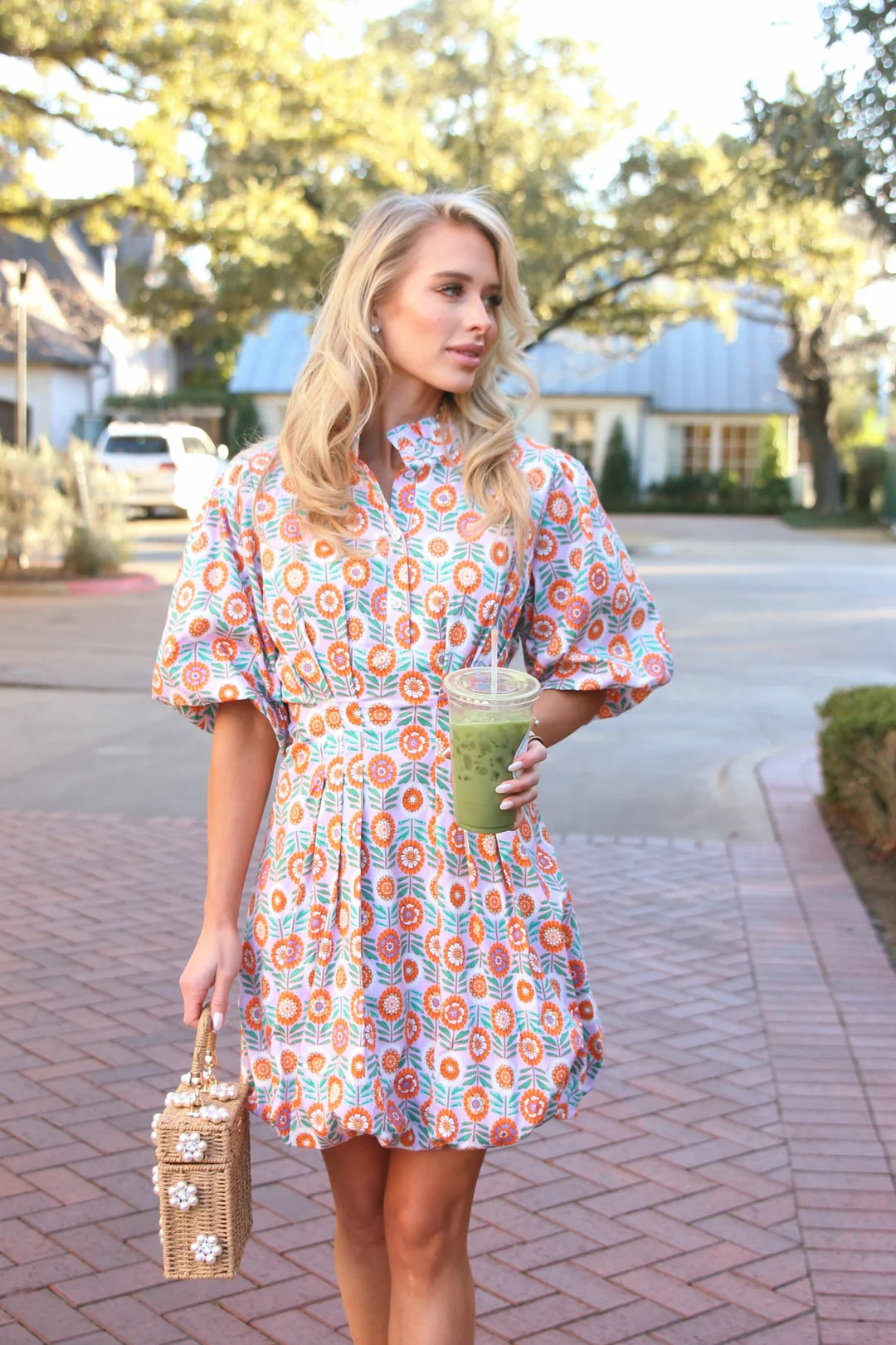 Woman in a colorful dress holding a drink and a bag on a sidewalk.