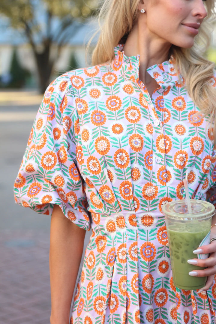 Woman in a floral dress holding a green smoothie outdoors.
