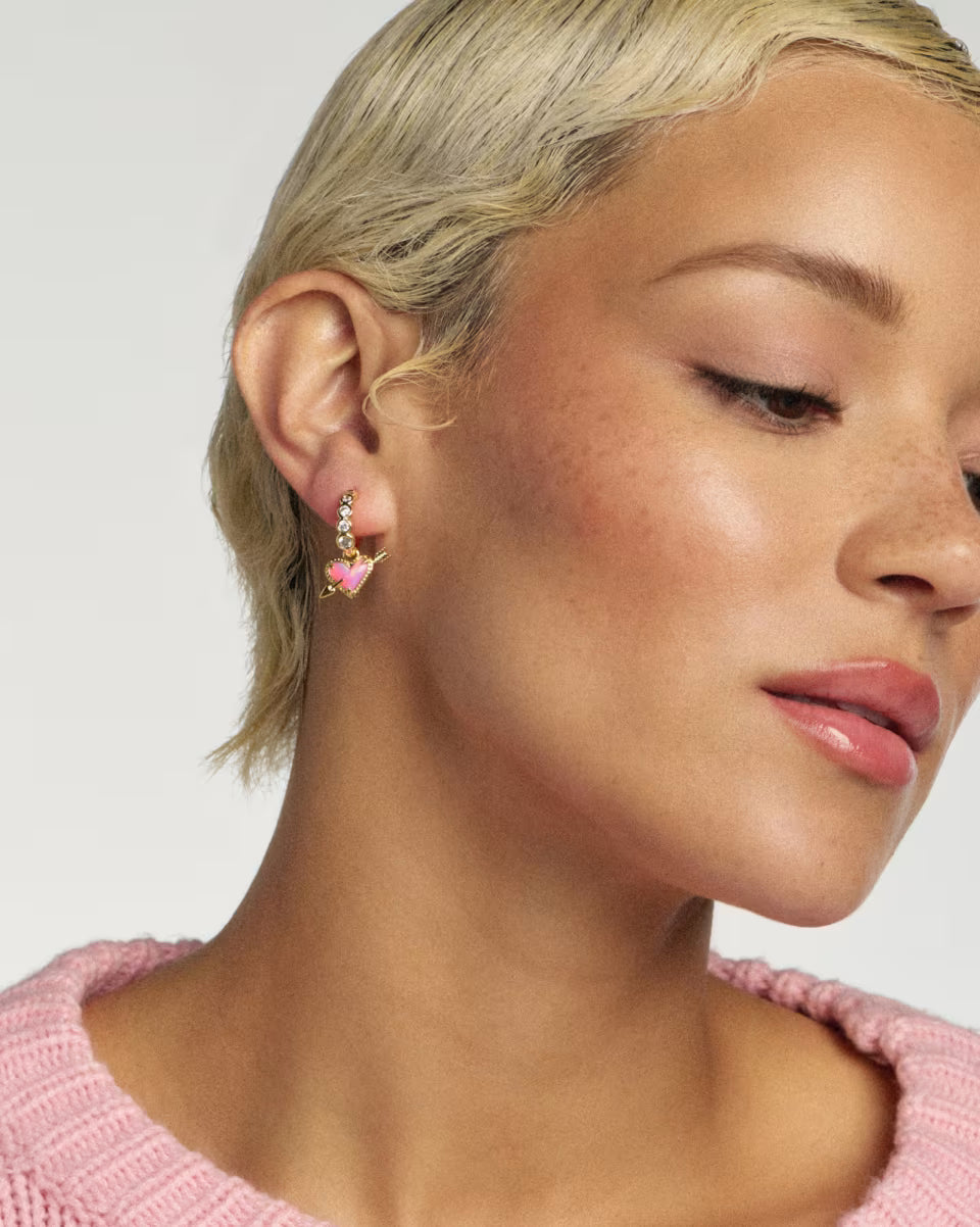 Close-up of a woman wearing earrings with a pink sweater on a light background
