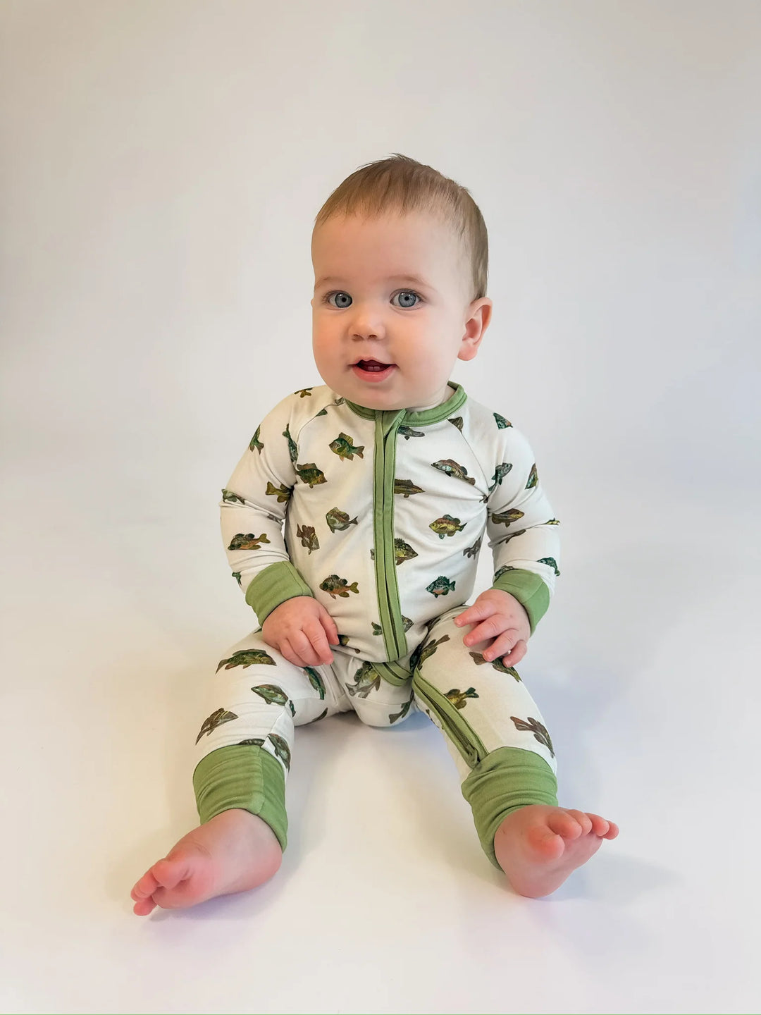 Baby wearing a green and white onesie with a fish pattern on a white background