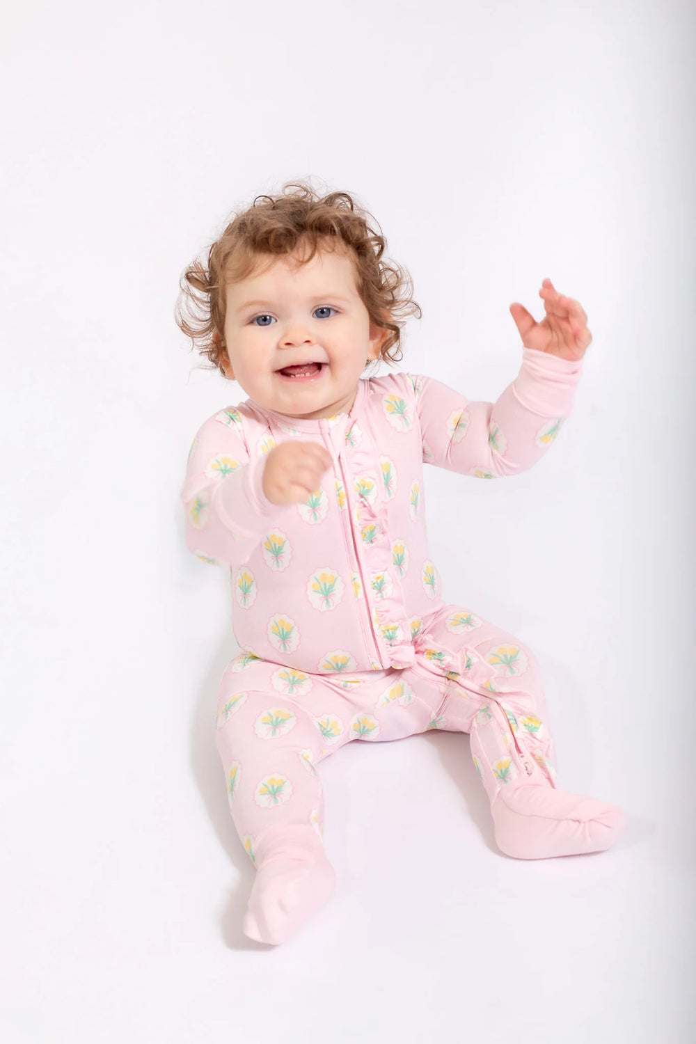 Baby in a pink floral onesie sitting on a white background