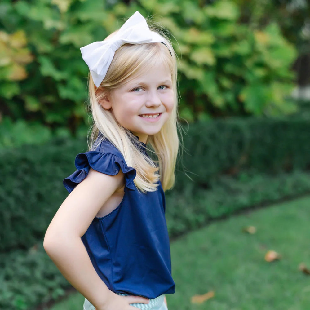 Young girl wearing a blue top and white bow in a park setting