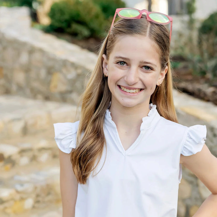 Young girl with sunglasses on her head, wearing a white shirt, outdoors.