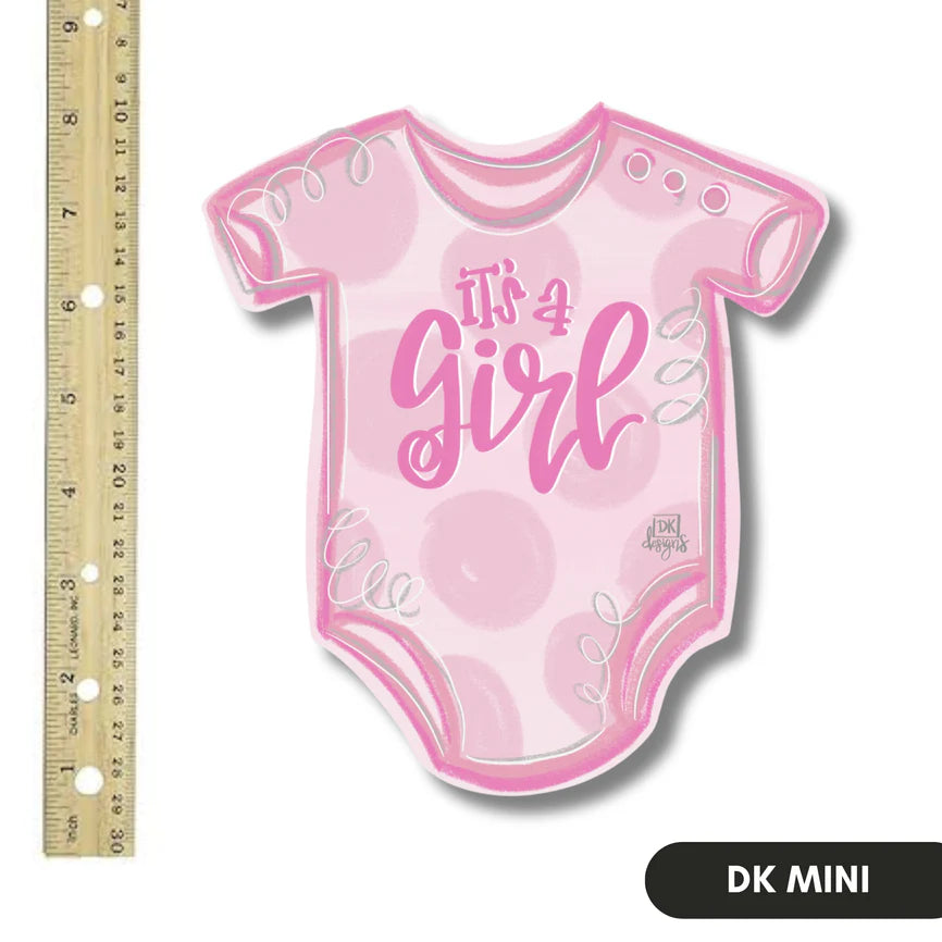 Pink baby onesie-shaped sign with 'It's a Girl' text next to a ruler for scale on a white background.