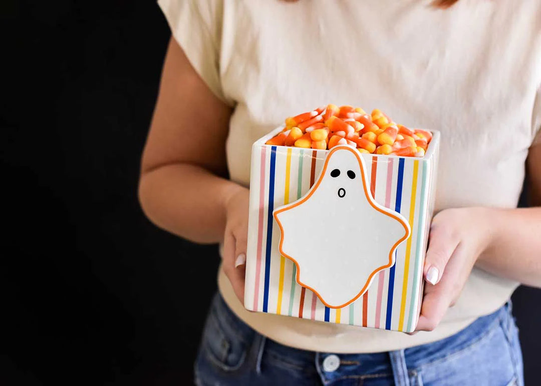 Person holding a striped ghost-shaped container filled with candy corn against a black background