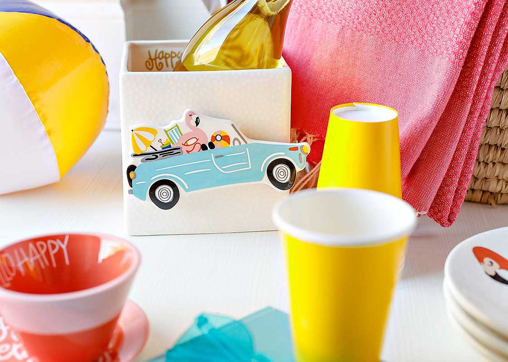 Colorful tableware including yellow cups, a red bowl, and a beach ball on a white surface.
