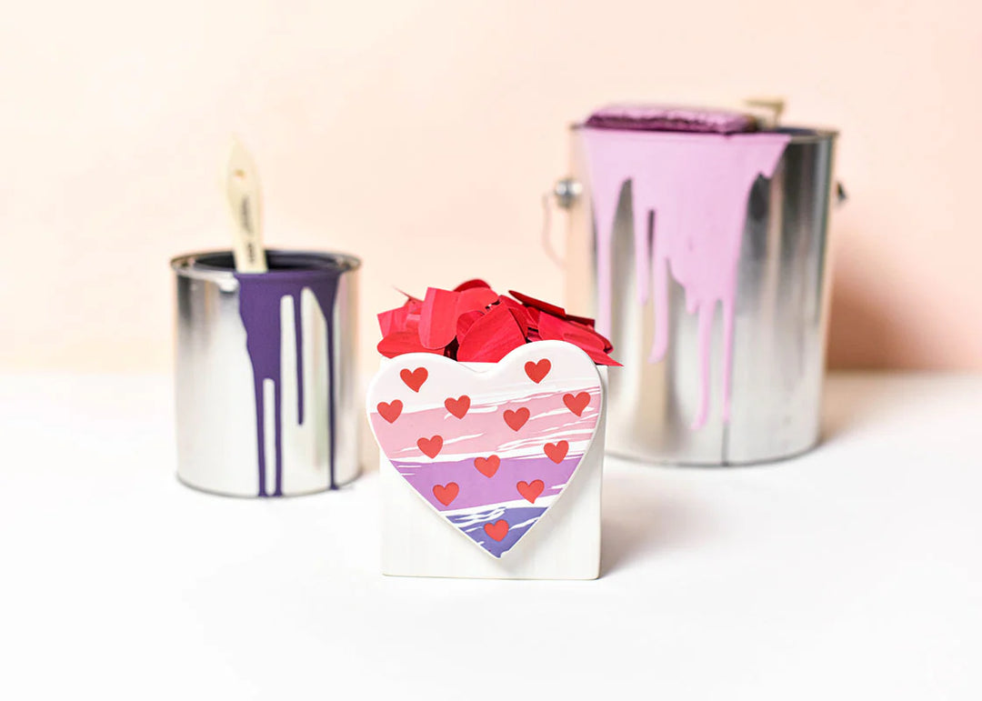 Heart-shaped box with red hearts and two metallic paint cans on a light background