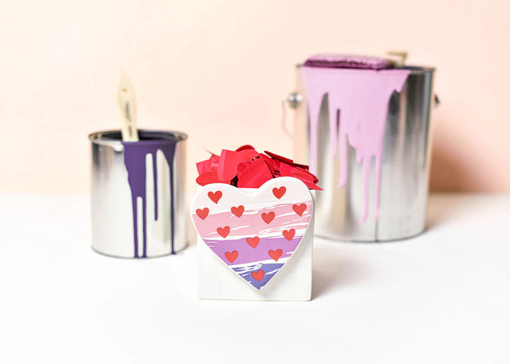 Heart-shaped box with red hearts and two metallic paint cans on a light background