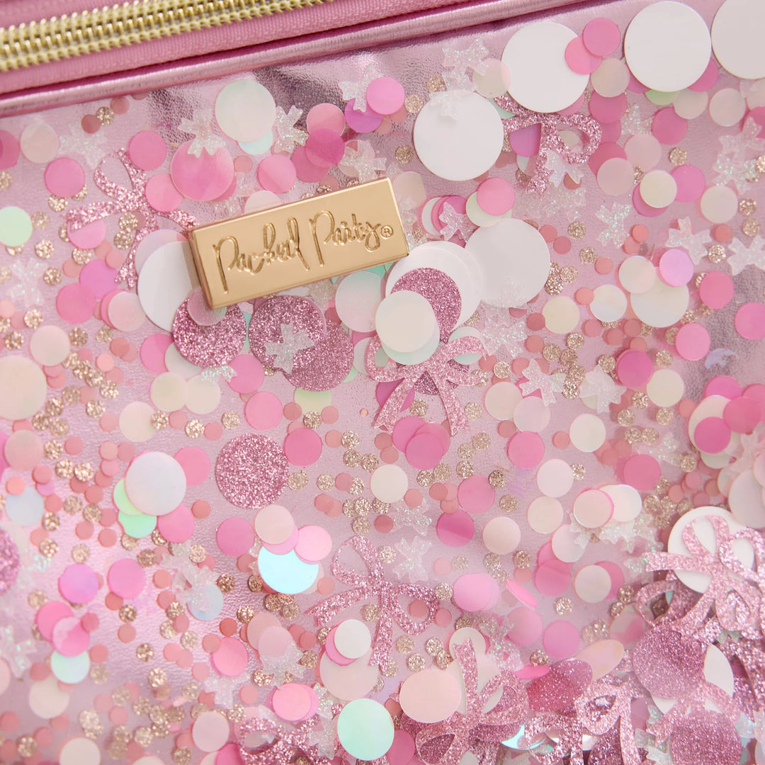 A close-up of a clear cosmetic pouch filled with pink and white confetti, glitter, and pastel pieces, with a gold zipper along the top and a gold tag reading 'Peachy Designs'.