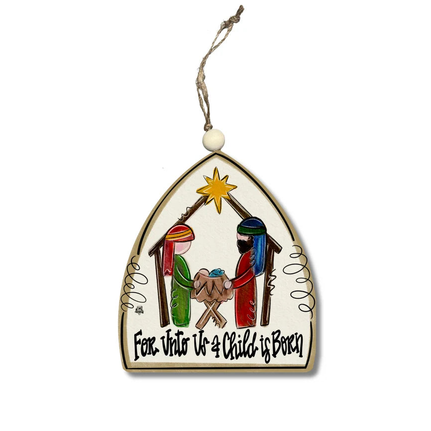 A Christmas nativity ornament shaped like a house with a hanging string and white bead. The ornament features a hand-painted scene of the Holy Family, baby Jesus, and wise men under a gold star, with the text 'For Unto Us A Child Is Born' written at the bottom.