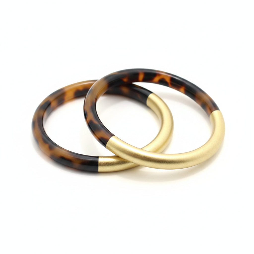 A circular bangle bracelet featuring a split design with a glossy tortoiseshell pattern on the top half and a smooth gold-toned finish on the bottom half, shown against a plain white background.