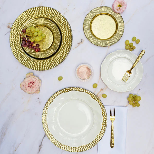 Elegant table setting with gold and white plates, forks, and decorative flowers on a marble surface.