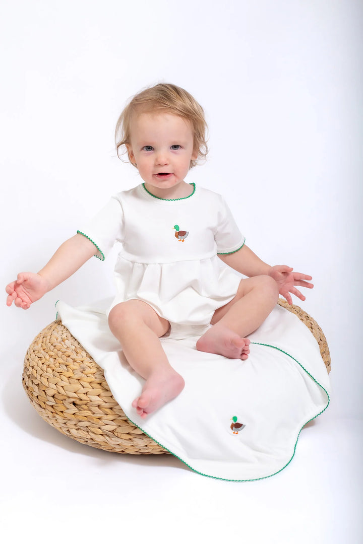 Child sitting on a woven stool with a white bubble featuring green trim and mallard design.