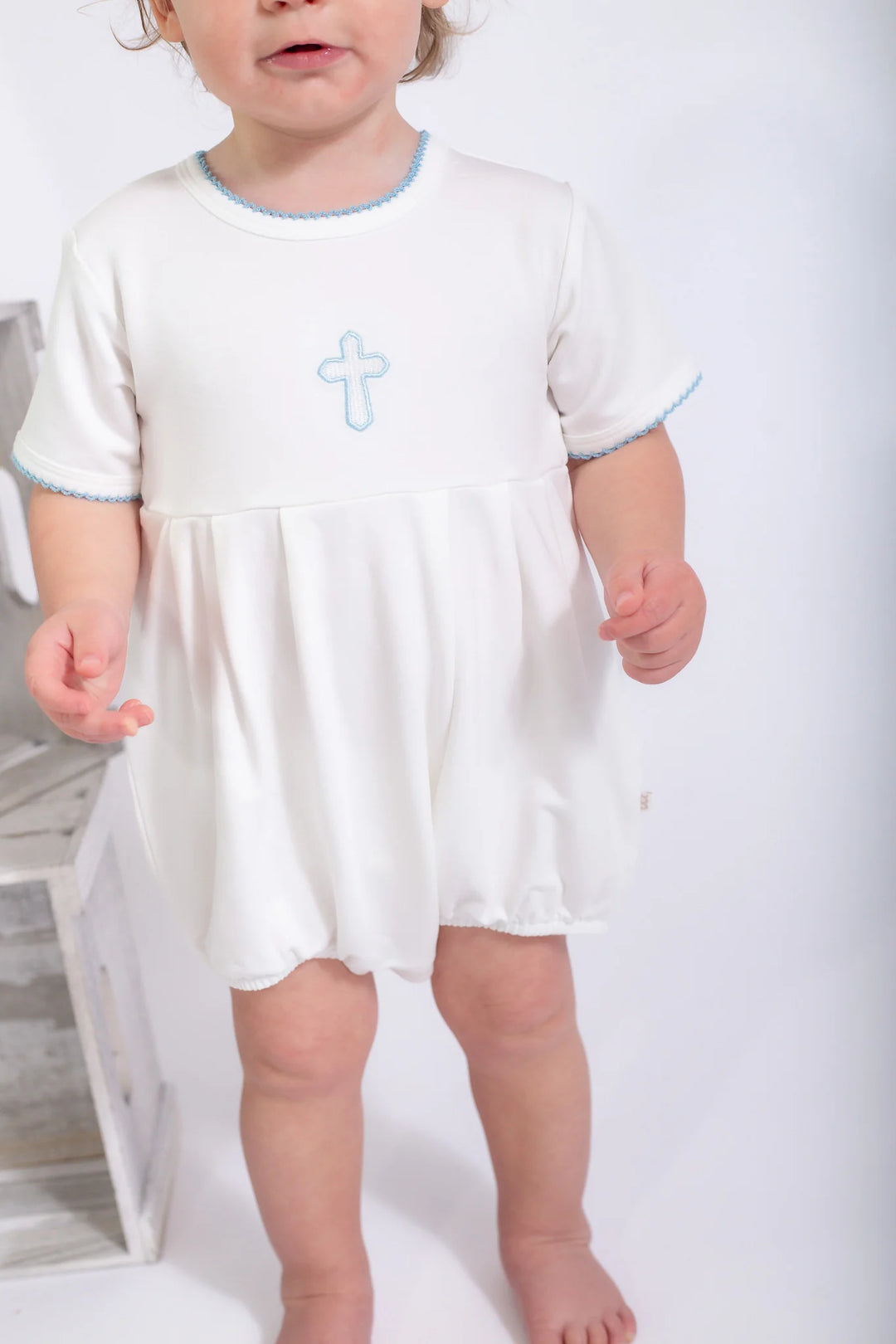 Child wearing a white dress with a blue cross on a plain background