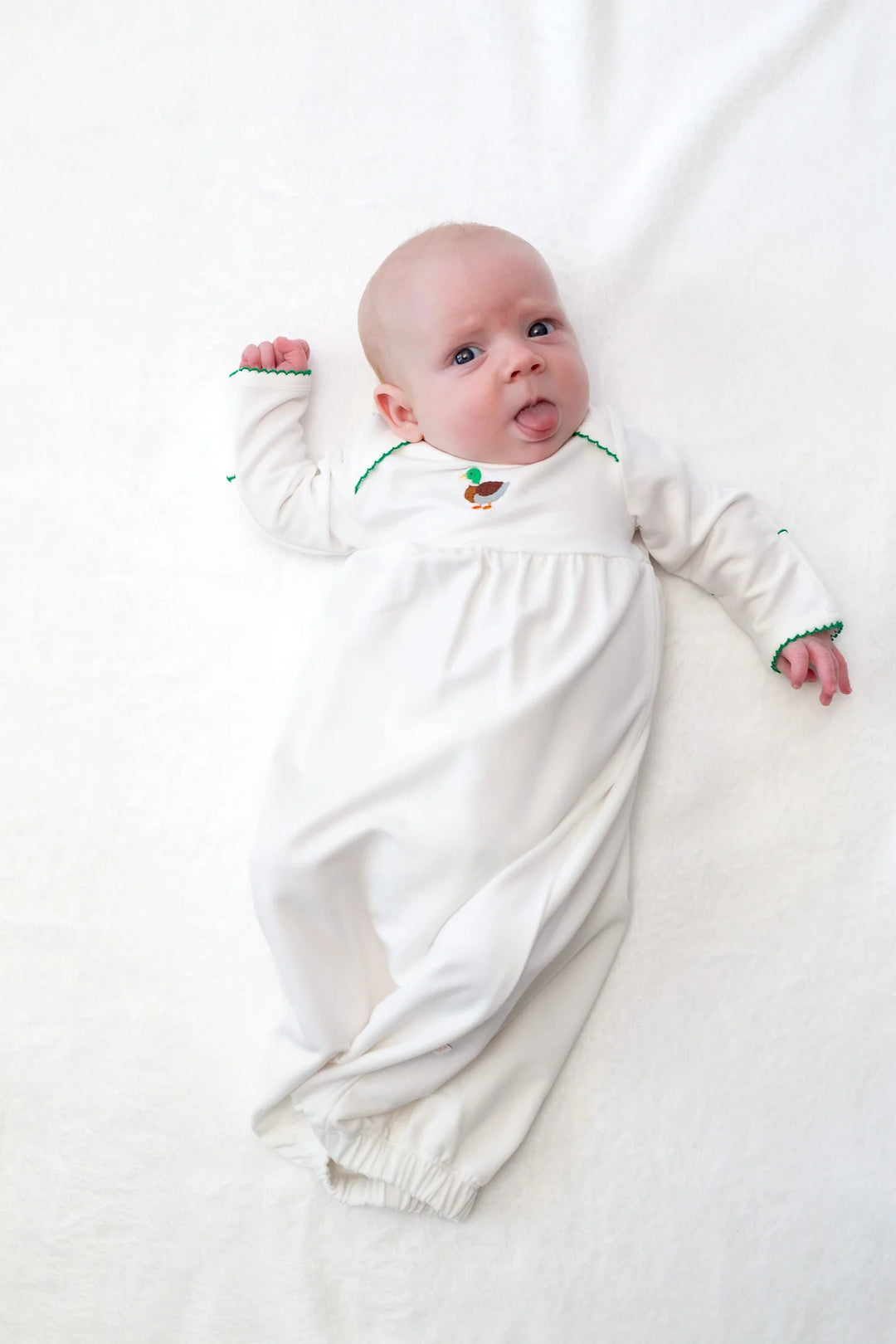 Baby in a white gown with green trim and duck motif on a white background