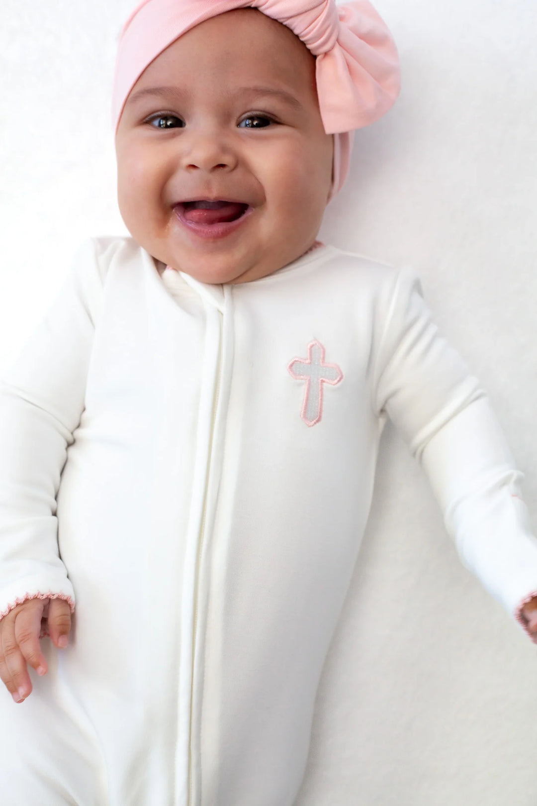 Baby wearing a white onesie with a pink cross design and a matching pink headband.