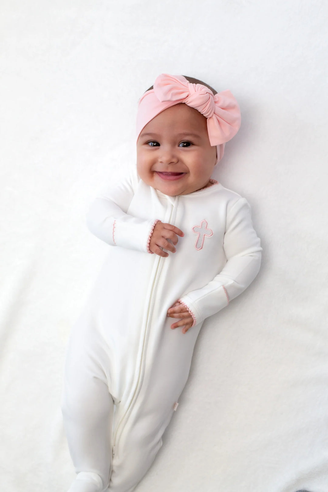 Baby in a white onesie with a pink bow headband on a white background