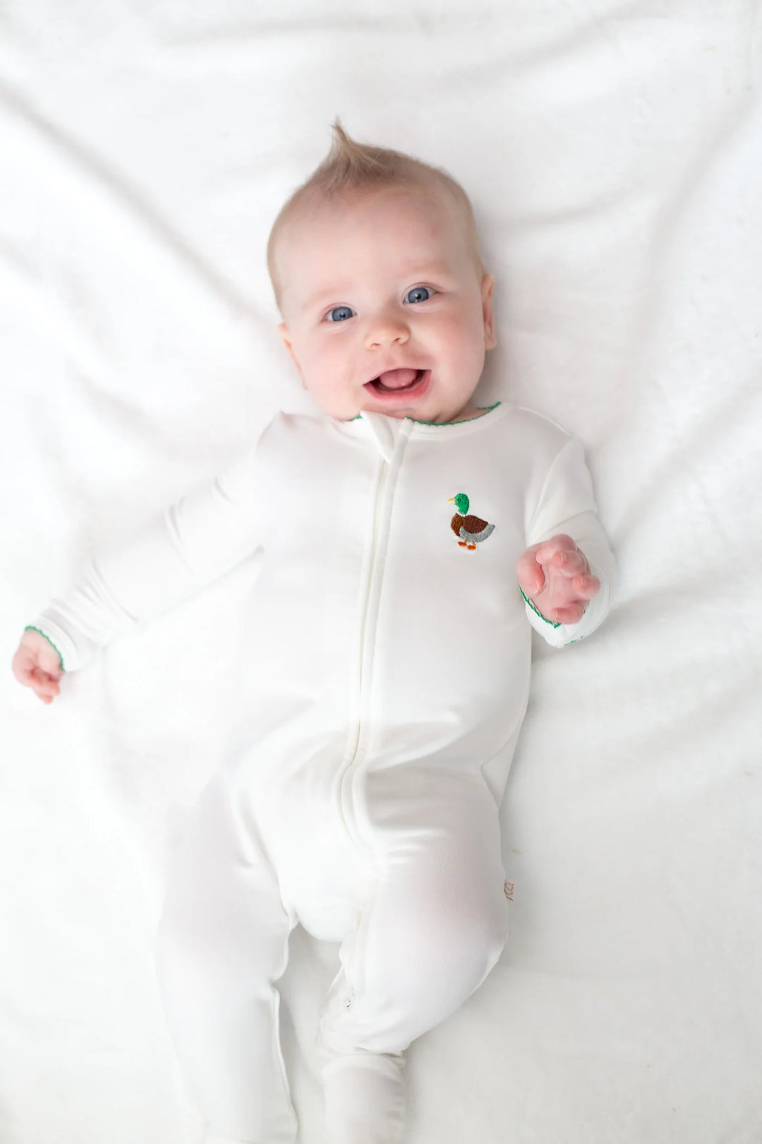 Baby wearing a white footie with a small mallard motif design on a white background