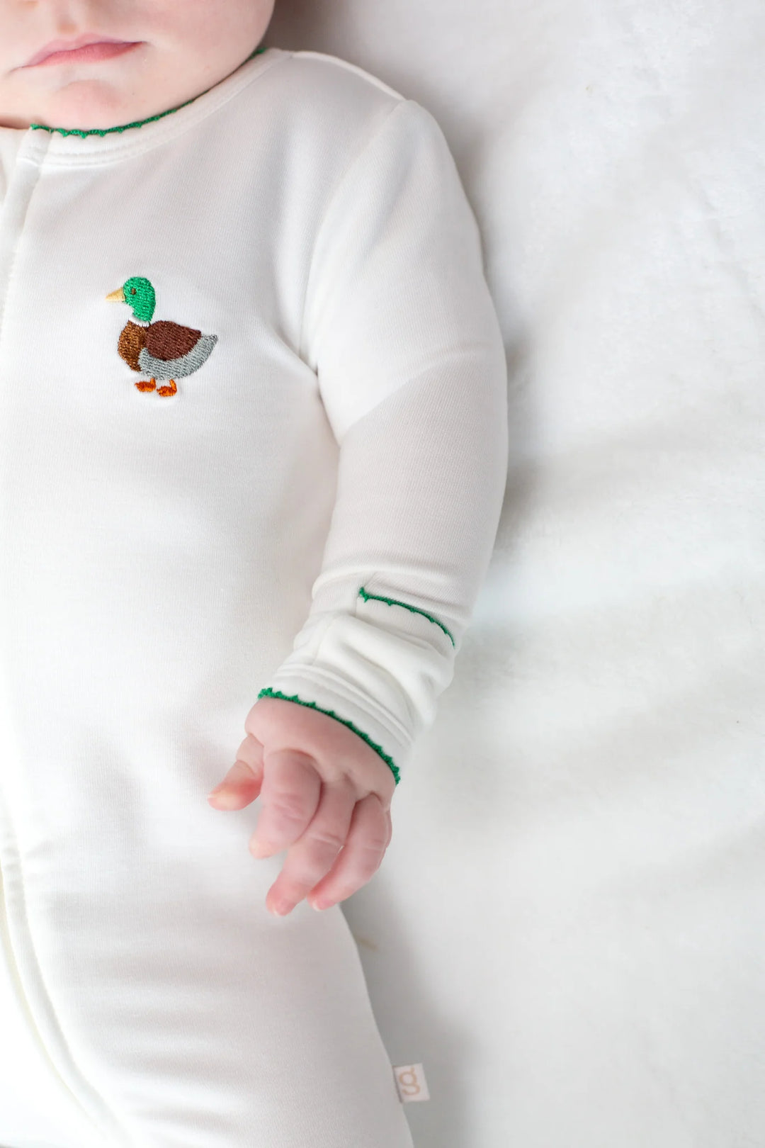 Baby wearing a white long-sleeve footie with a duck design on a white background