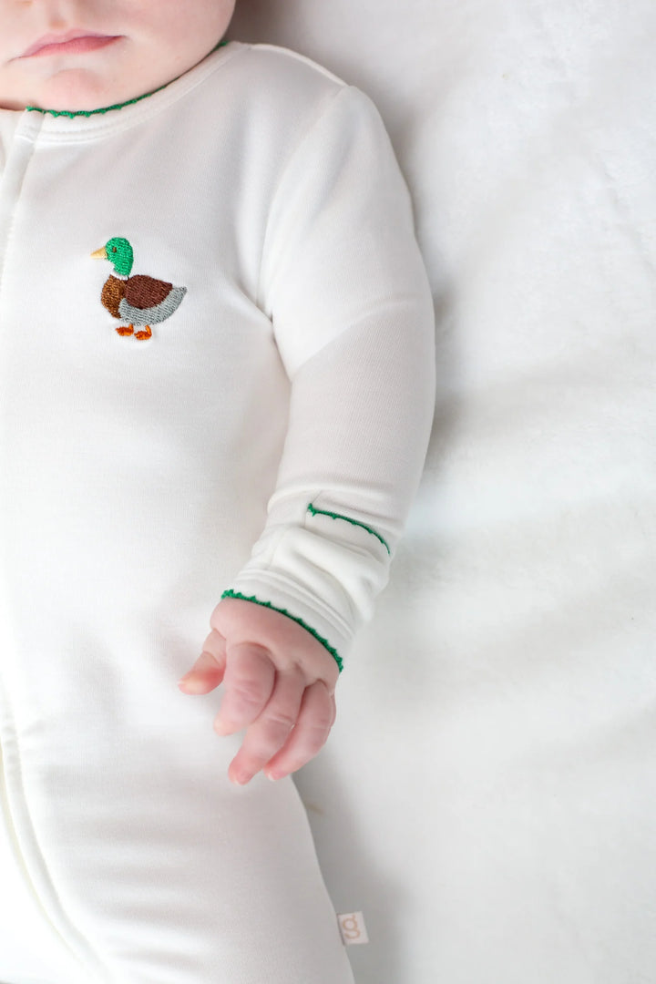 Baby wearing a white long-sleeve footie with a duck design on a white background