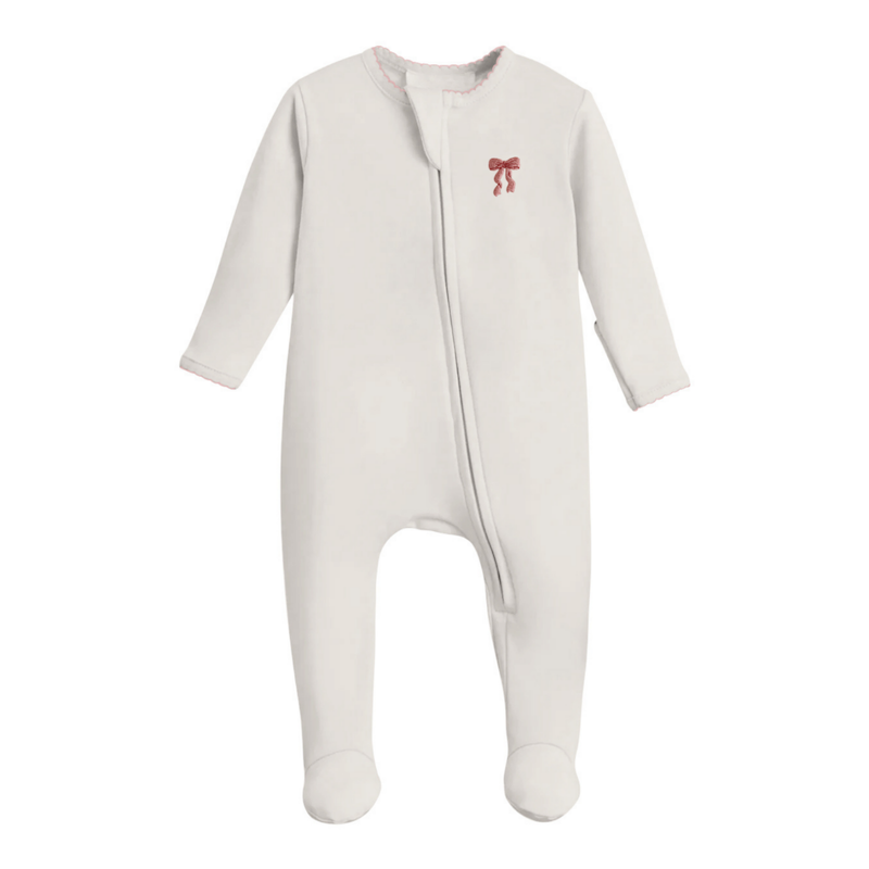 A baby footed sleeper in off-white with a small red bow graphic on the left chest, displayed against a solid white background.