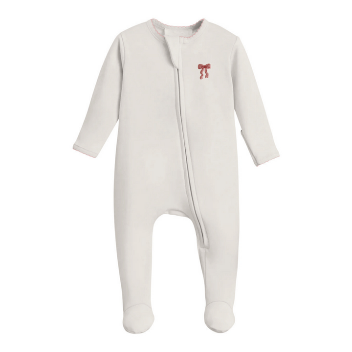 A baby footed sleeper in off-white with a small red bow graphic on the left chest, displayed against a solid white background.