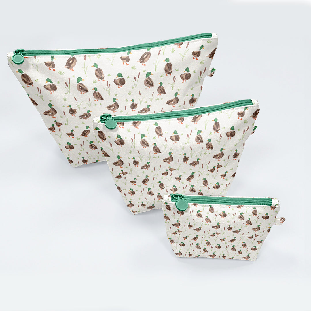 Three pouches with duck pattern and green zippers on a light gray background