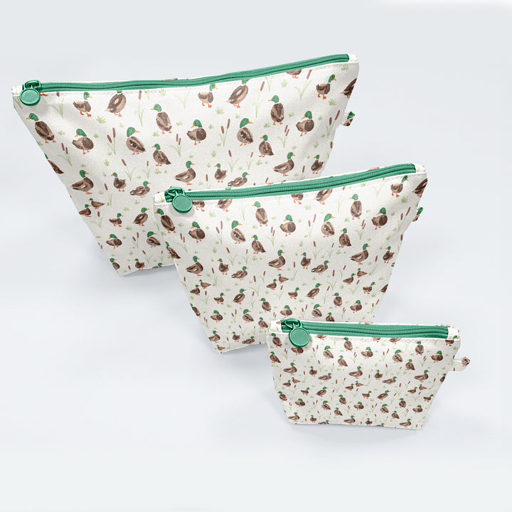 Three pouches with duck pattern and green zippers on a light gray background