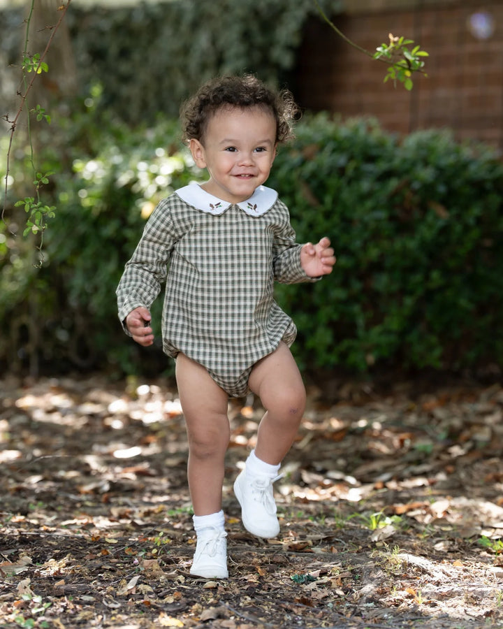 Child in a checkered outfit running outdoors with greenery in the background