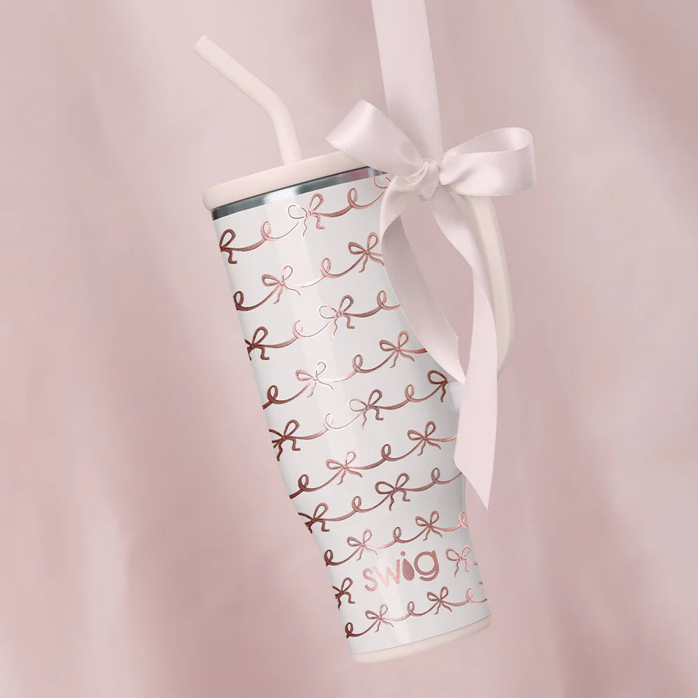 Tumbler with rose gold text and a white ribbon on a pink background