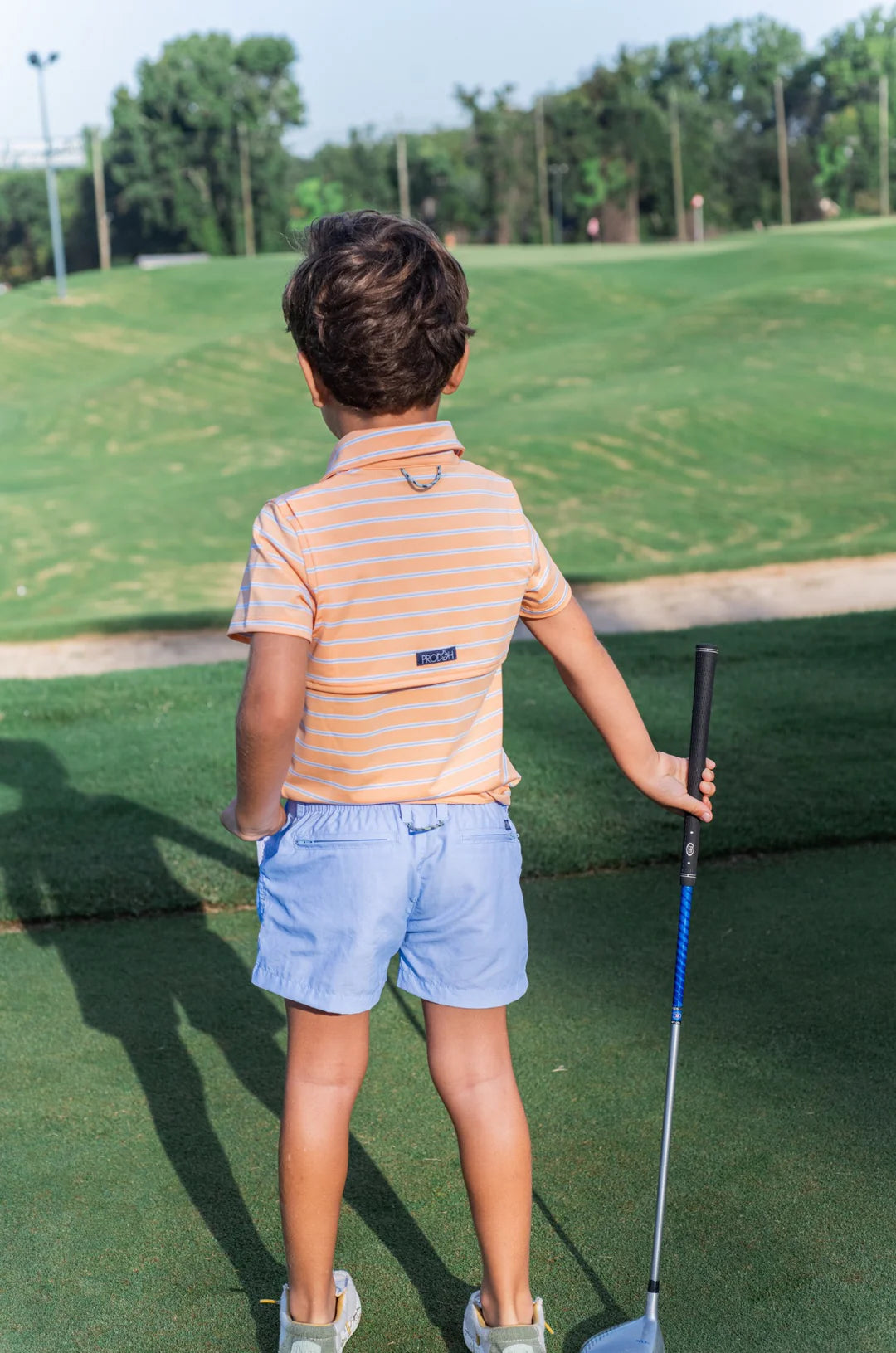 LITTLE BOY AT GOLF COURSE WEARING ORANGE AND  BLUE STRIPE BOYS SHORT SLEEVE POLO WITH COLLAR
