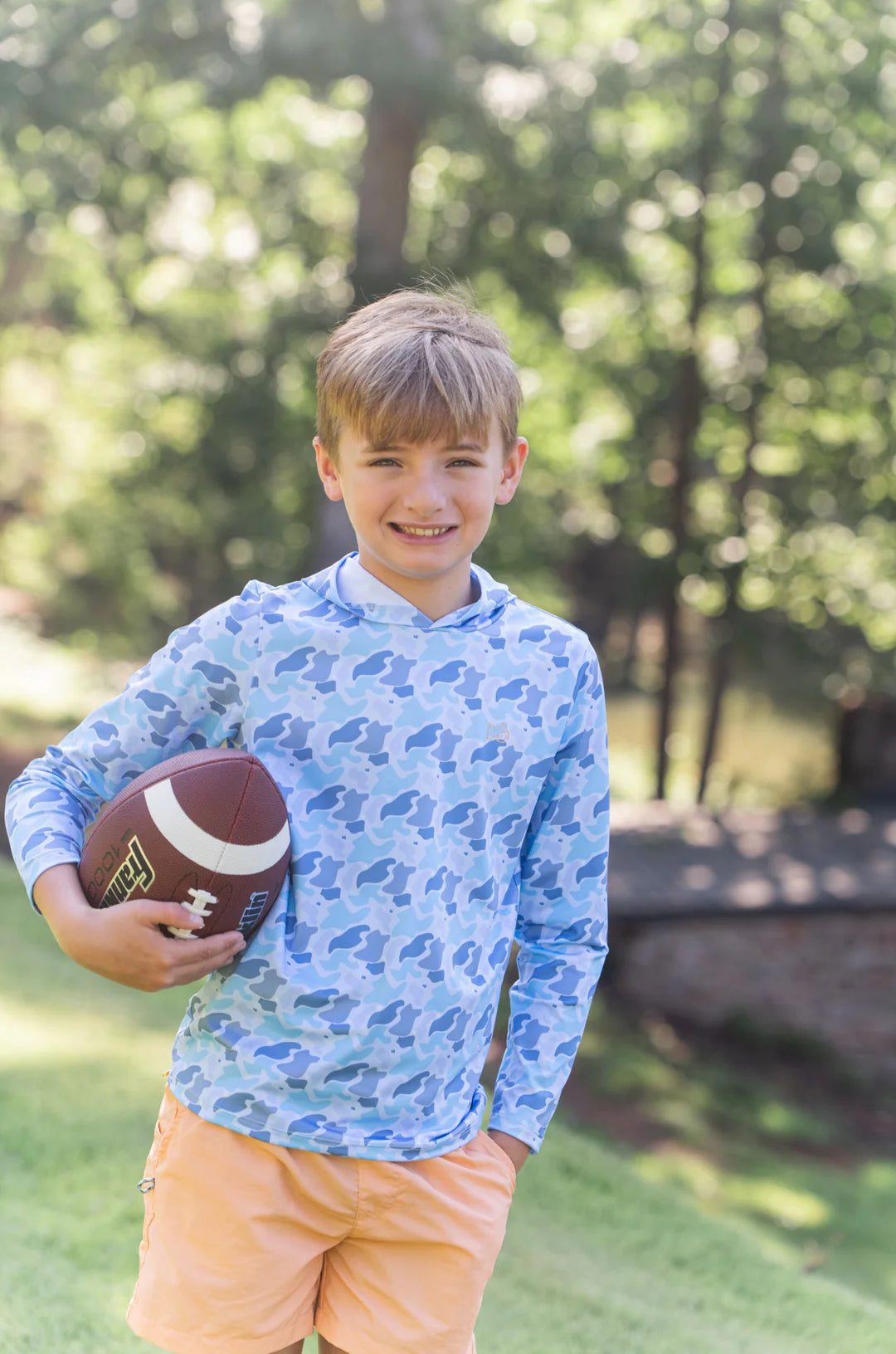 LITTLE BOY IN ORANGE SHORTS AND BLUE CAMO HOODIE WITH FOOTBALL