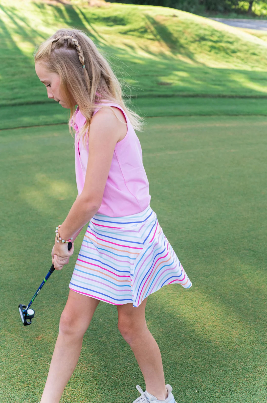 GIRL WEARING PINK TANK TOP AND STRIPED GOLF SKIRT ON GOLF COURSE WITH GOLF CLUB