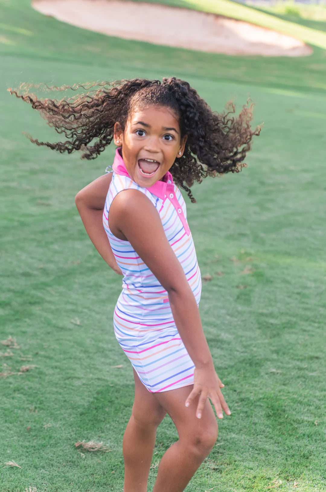 GIRL WEARING GIRLS SLEEVELESS MULTICOLOR STRIPED DRESS WITH PINK COLLAR ON GOLF COURSE