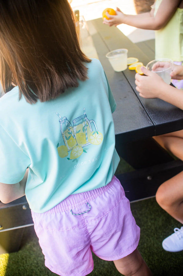 LITTLE GIRL IN PINK SHORTS AND LIGHT BLUE SHORT SLEEVE T-SHIRT WITH LEMONADE PAINTING ON BACK