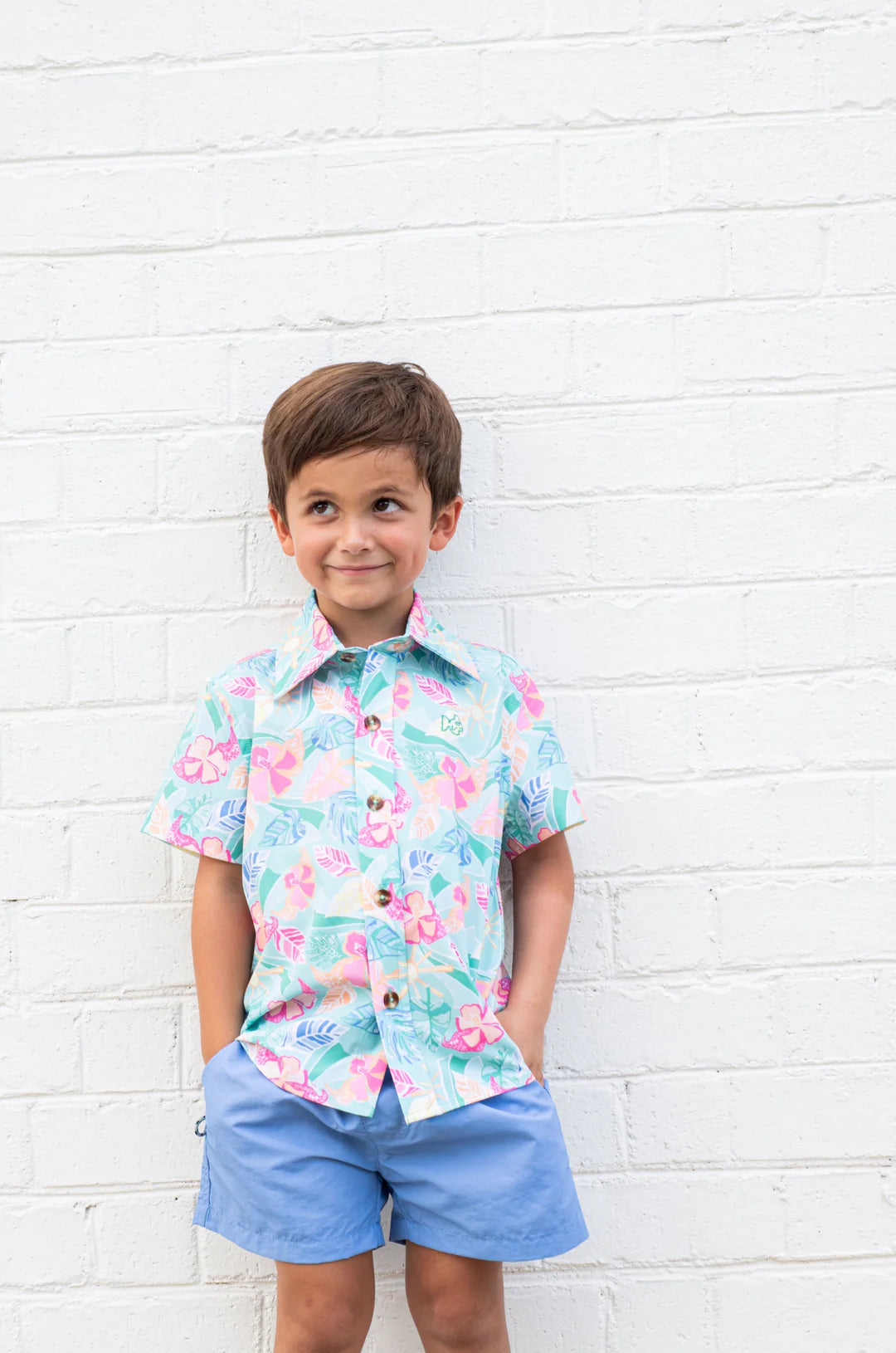 LITTLE BOY WITH FLORAL PRINT SHORT WITH BLUE SHORTS AGAINST WHITE BRICK WALL