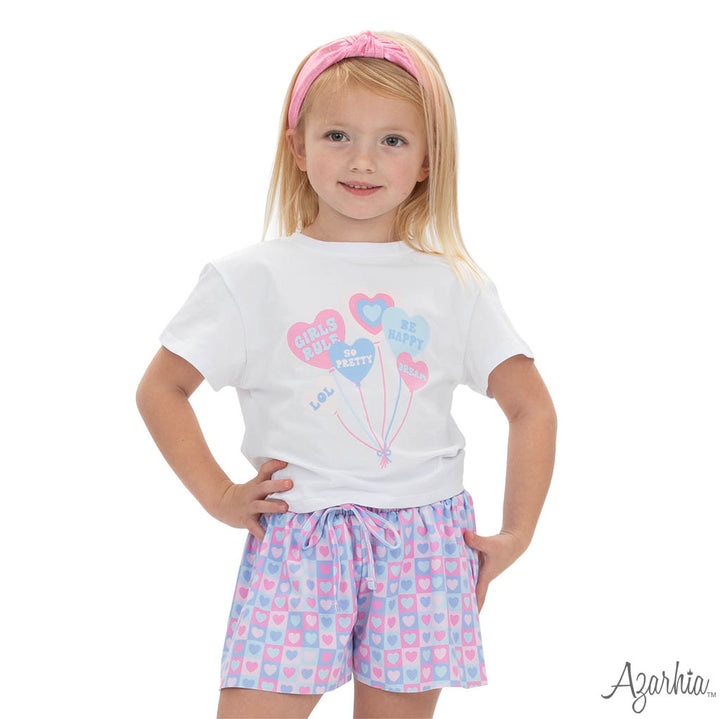 Young girl wearing a white t-shirt with balloon design and checkered shorts on a white background