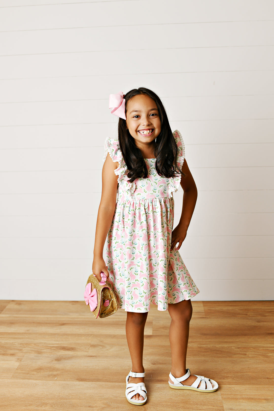 Young girl in a floral dress standing on a wooden floor with a white background