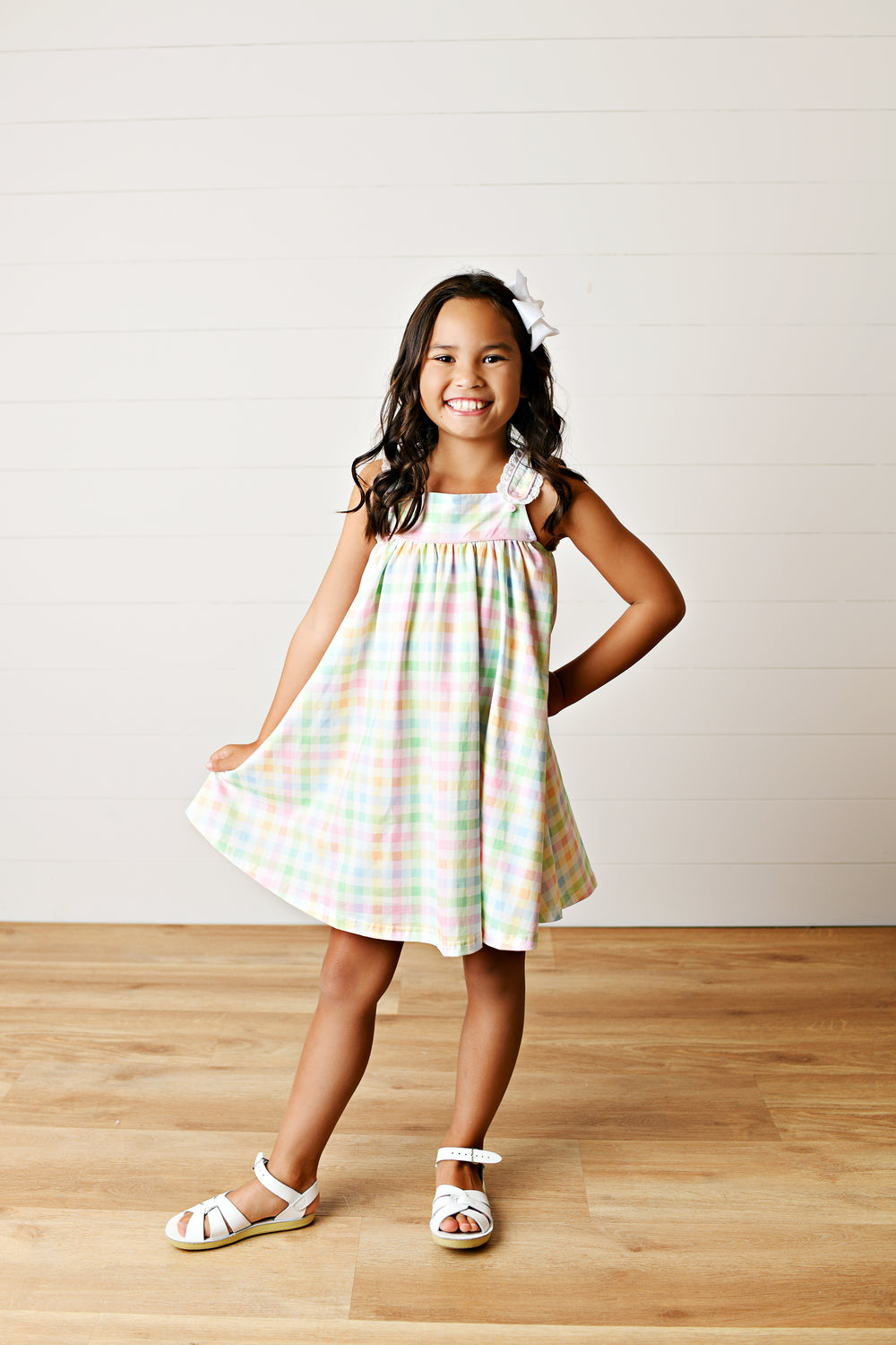 Young girl wearing a colorful dress standing on a wooden floor with a white wall background