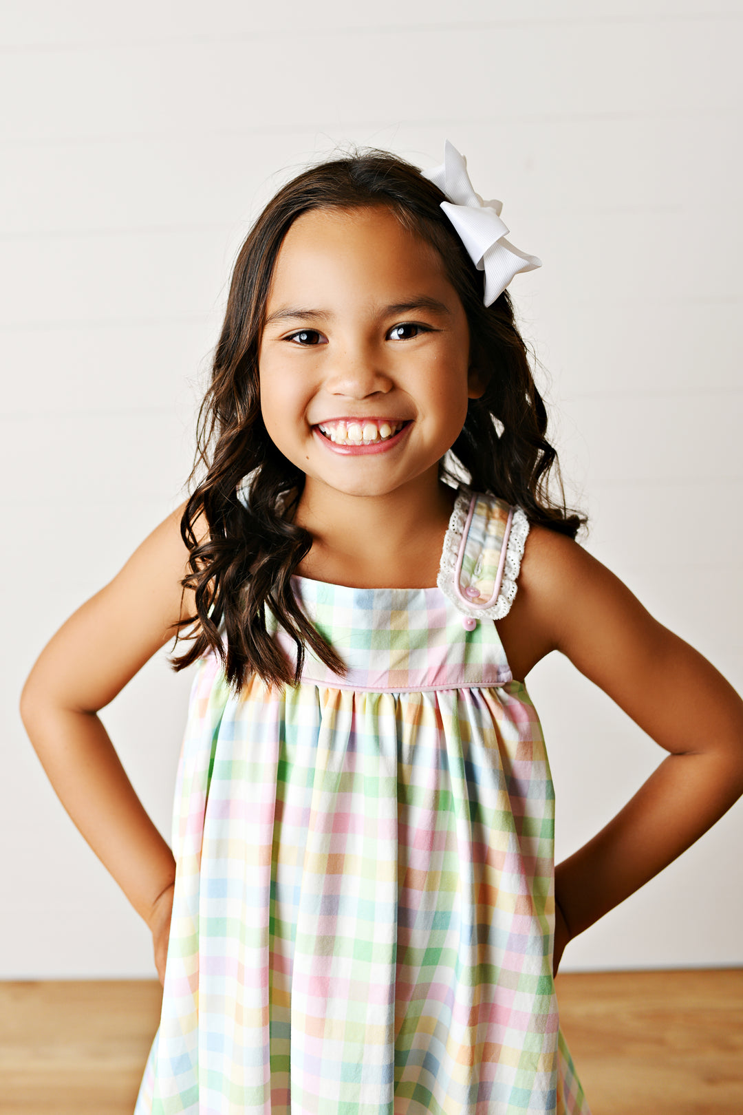 Young girl wearing a colorful dress with a white bow in her hair, standing against a plain background.