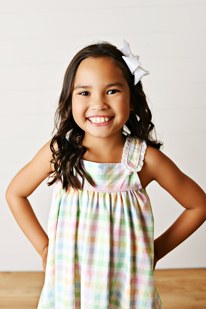 Young girl wearing a colorful dress with a white bow in her hair, standing against a plain background.