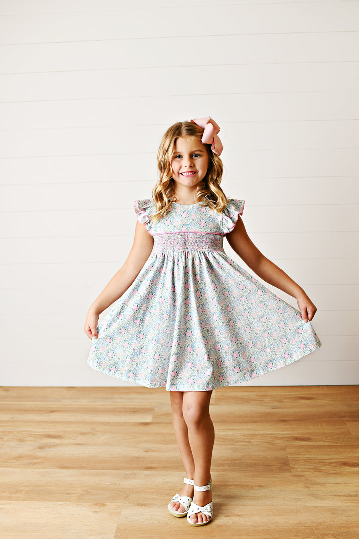 Young girl wearing a floral dress on a wooden floor with a white wall background