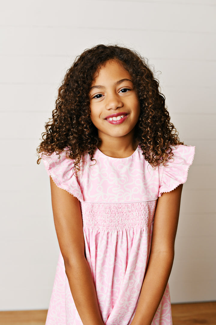 Young girl wearing a pink dress with ruffled sleeves against a plain background