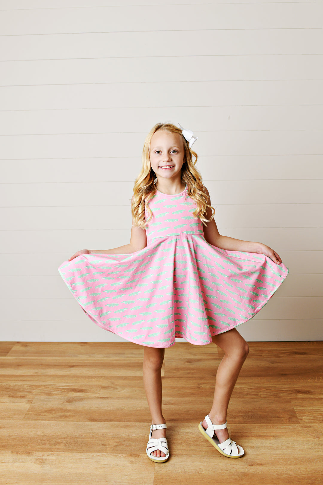Young girl in a pink dress with white polka dots standing on a wooden floor.