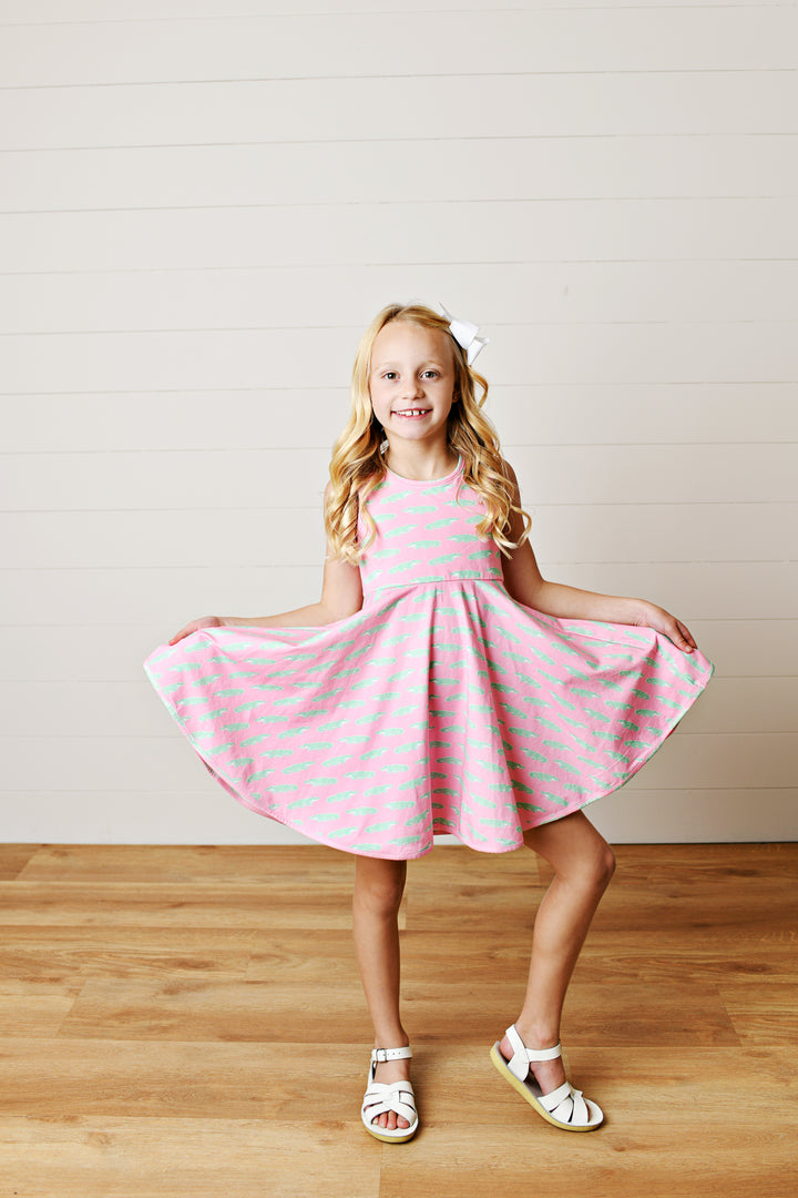 Young girl in a pink dress with white polka dots standing on a wooden floor.