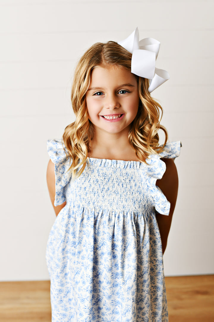 Young girl wearing a floral dress with ruffled sleeves and a large white bow in her hair.