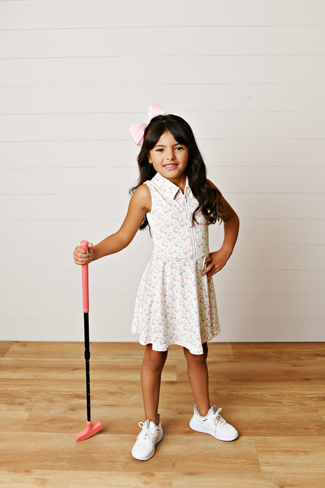 Young girl in a white dress holding a pink and black club on a wooden floor.
