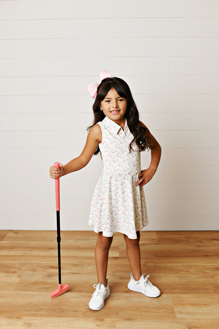 Young girl in a white dress holding a pink and black club on a wooden floor.